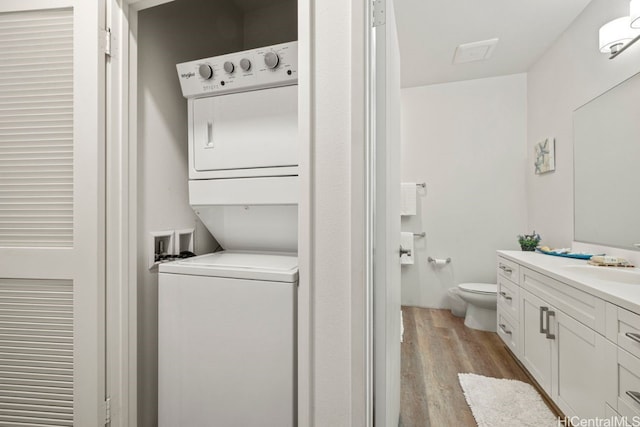 bathroom with hardwood / wood-style flooring, vanity, toilet, and stacked washer and clothes dryer