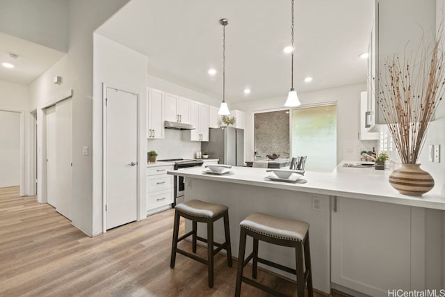 kitchen featuring appliances with stainless steel finishes, a breakfast bar, pendant lighting, light hardwood / wood-style flooring, and white cabinetry