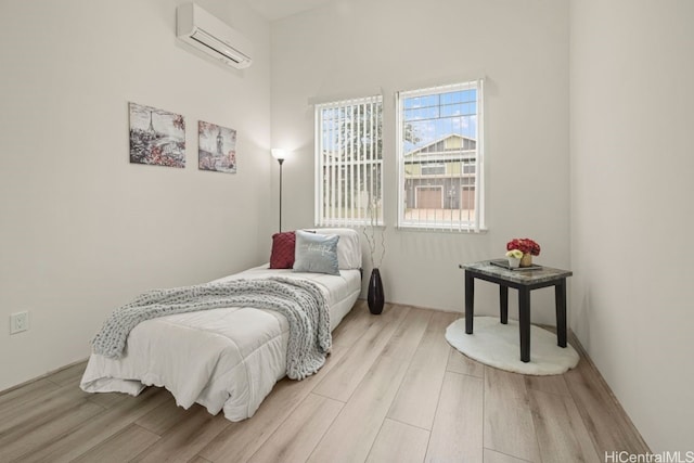 bedroom with a wall mounted AC and light hardwood / wood-style flooring