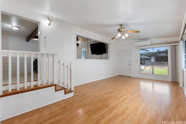 interior space with a wall mounted air conditioner, ceiling fan, beamed ceiling, and light hardwood / wood-style flooring