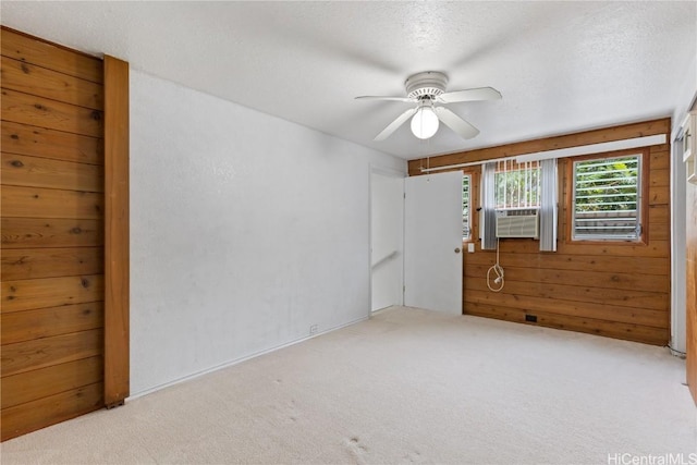 carpeted empty room featuring a textured ceiling, wooden walls, ceiling fan, and cooling unit