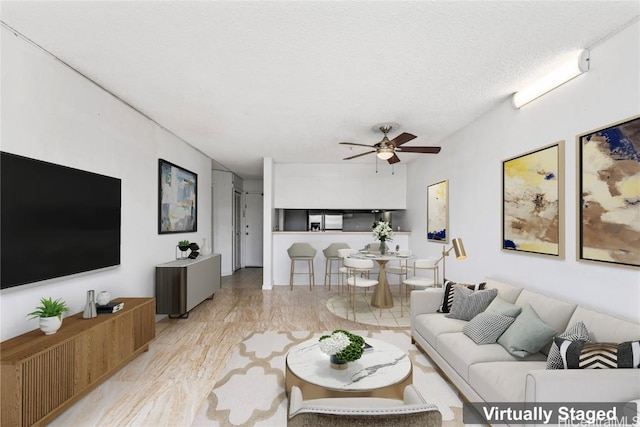 living room featuring ceiling fan, light wood-type flooring, and a textured ceiling