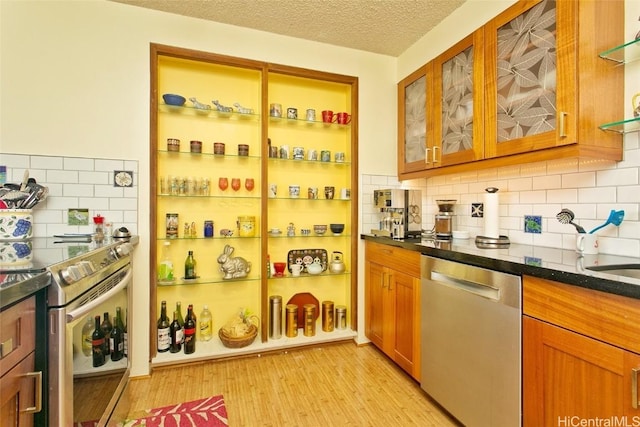 interior space featuring decorative backsplash, appliances with stainless steel finishes, dark stone counters, a textured ceiling, and light hardwood / wood-style floors