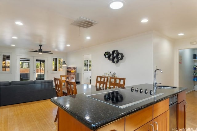 kitchen featuring an island with sink, black electric cooktop, light wood-type flooring, ceiling fan, and sink