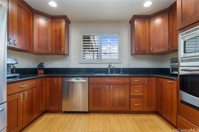 kitchen with stainless steel appliances, dark stone counters, light hardwood / wood-style flooring, and sink