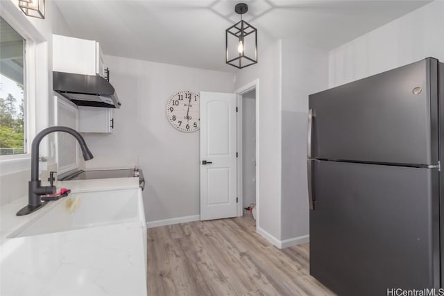 kitchen with pendant lighting, sink, white cabinetry, light wood-type flooring, and black refrigerator