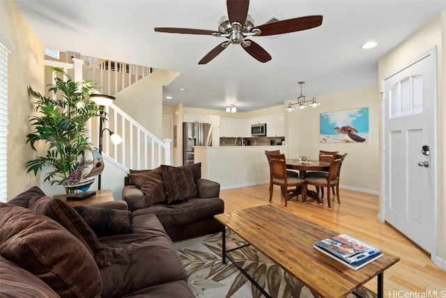 living room with ceiling fan with notable chandelier and light hardwood / wood-style floors