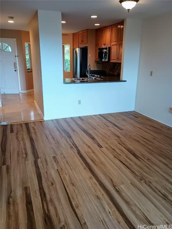 kitchen with sink, light hardwood / wood-style flooring, appliances with stainless steel finishes, kitchen peninsula, and decorative backsplash