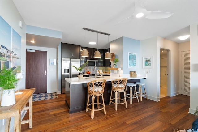 kitchen featuring appliances with stainless steel finishes, dark hardwood / wood-style floors, pendant lighting, a breakfast bar area, and backsplash