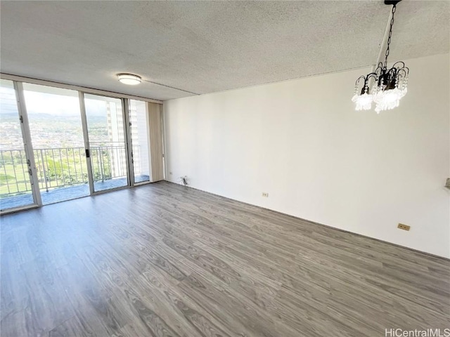 empty room featuring wood-type flooring, a wall of windows, a textured ceiling, and a chandelier