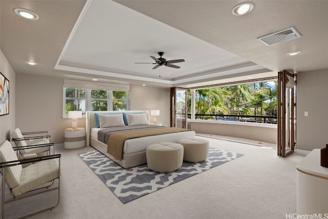 bedroom featuring ceiling fan, light colored carpet, and a tray ceiling