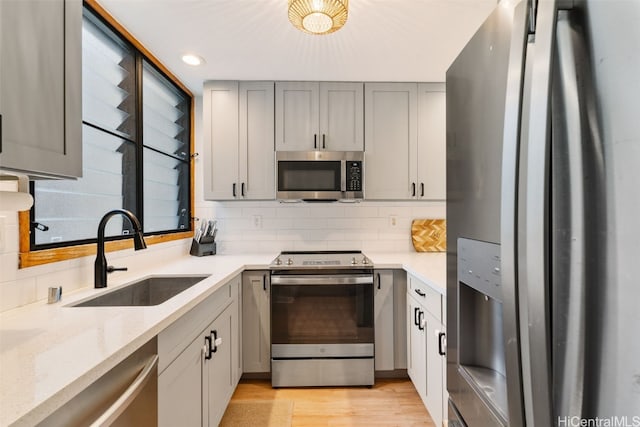 kitchen featuring gray cabinetry, sink, backsplash, stainless steel appliances, and light stone counters