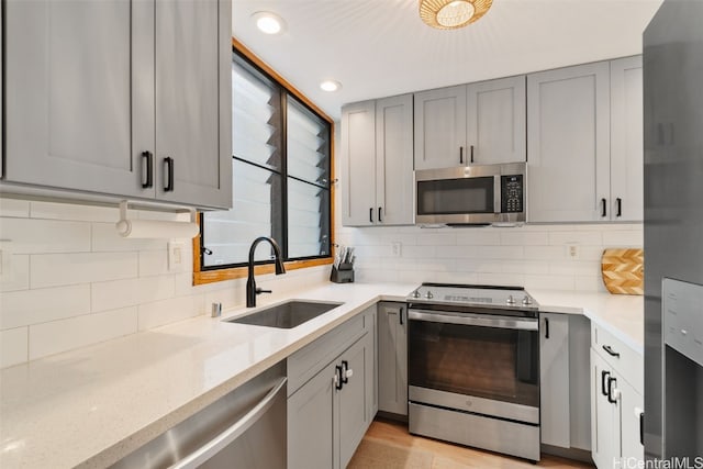 kitchen with appliances with stainless steel finishes, sink, tasteful backsplash, light stone countertops, and gray cabinets