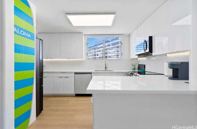 kitchen with kitchen peninsula, sink, white cabinetry, light wood-type flooring, and appliances with stainless steel finishes