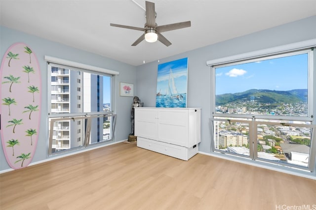 bedroom with light wood-type flooring, ceiling fan, a mountain view, and multiple windows