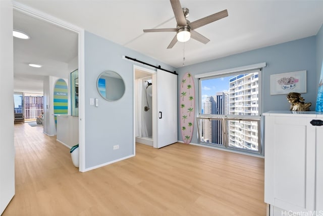 bedroom with ceiling fan, light hardwood / wood-style flooring, and a barn door