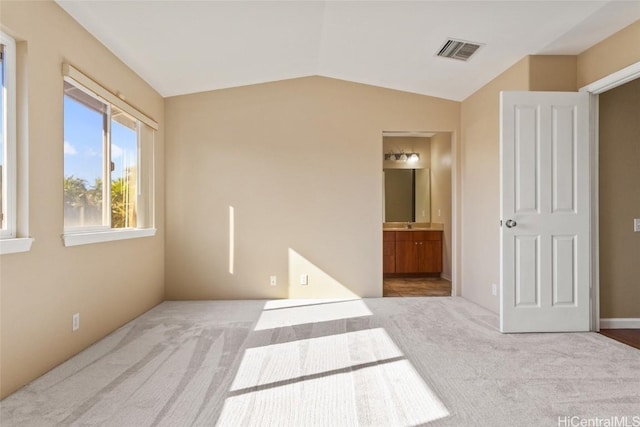 bedroom with lofted ceiling, light colored carpet, and ensuite bath