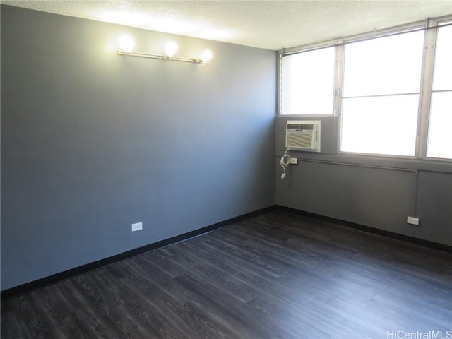 empty room featuring an AC wall unit, dark hardwood / wood-style flooring, and a textured ceiling