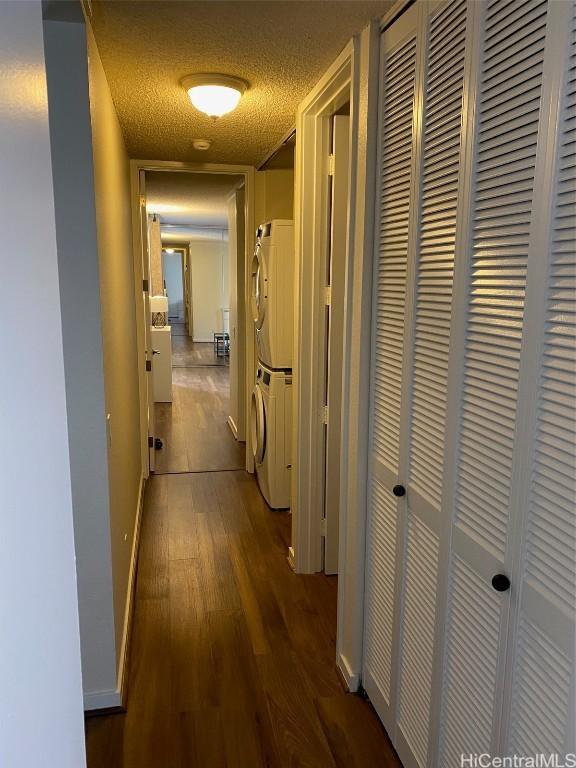 hall featuring dark hardwood / wood-style floors, a textured ceiling, and stacked washing maching and dryer