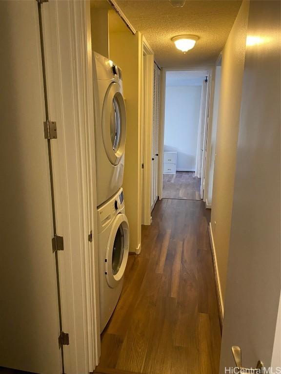 laundry room with stacked washer / dryer, dark wood-type flooring, and a textured ceiling