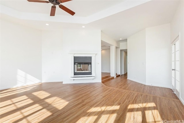 unfurnished living room with ceiling fan, a multi sided fireplace, and light wood-type flooring