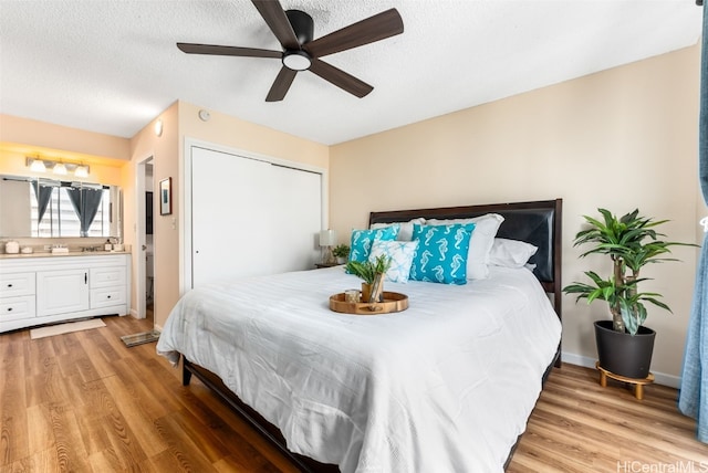 bedroom featuring ensuite bath, a textured ceiling, ceiling fan, wood-type flooring, and a closet