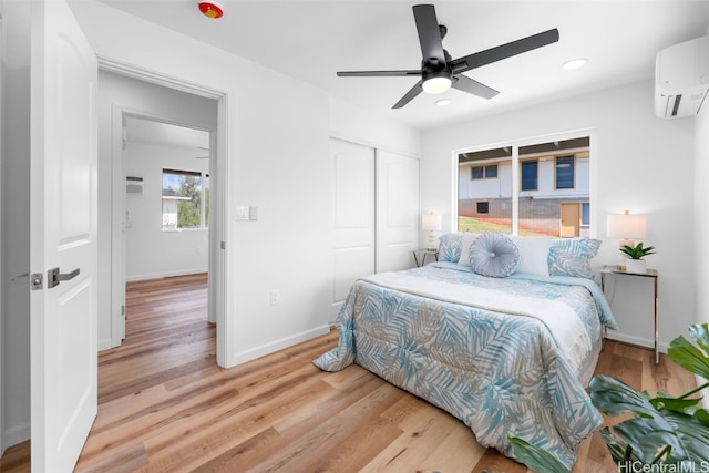 bedroom featuring light hardwood / wood-style floors, ceiling fan, a wall mounted air conditioner, and a closet