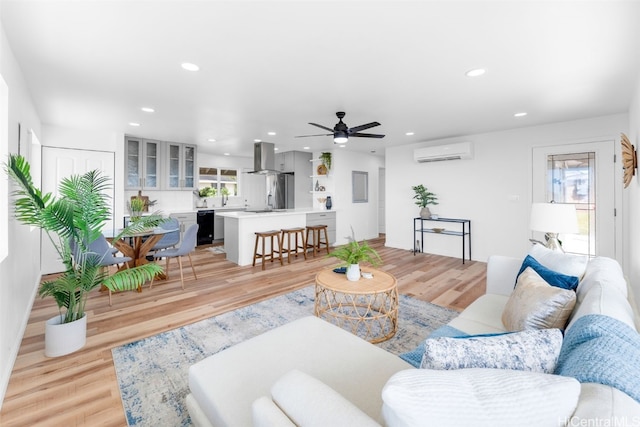 living room with a wall mounted AC, ceiling fan, light wood-type flooring, and sink