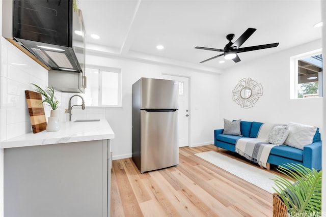 kitchen featuring light wood-type flooring, backsplash, stainless steel refrigerator, ceiling fan, and sink