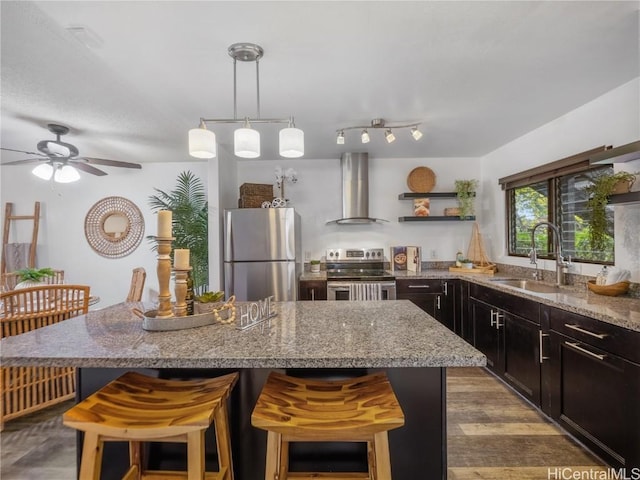 kitchen featuring a center island, a kitchen breakfast bar, wall chimney range hood, sink, and appliances with stainless steel finishes