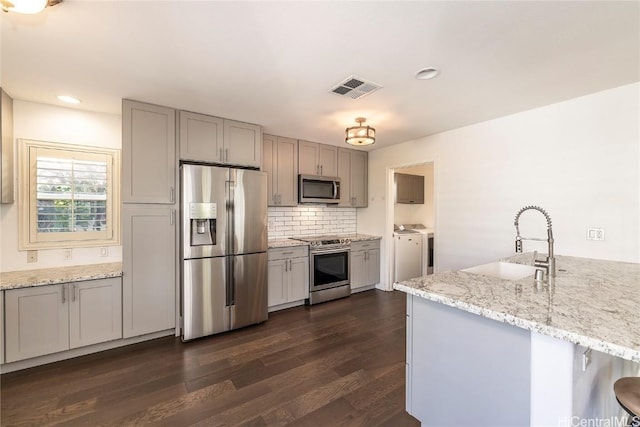 kitchen featuring kitchen peninsula, appliances with stainless steel finishes, light stone counters, sink, and separate washer and dryer