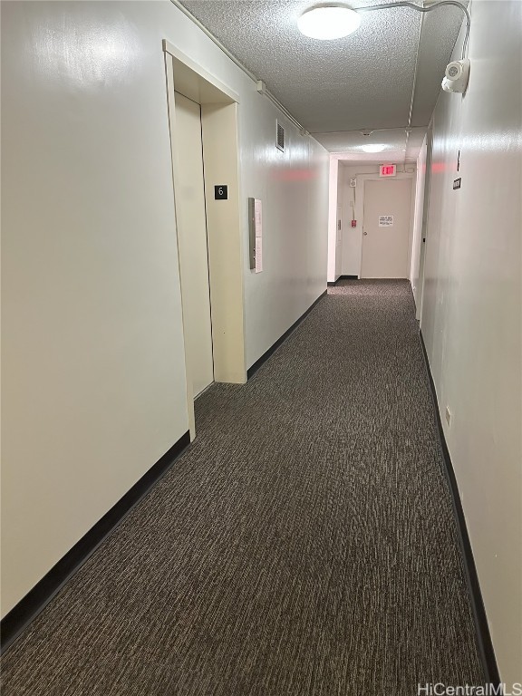 corridor with a textured ceiling and dark carpet