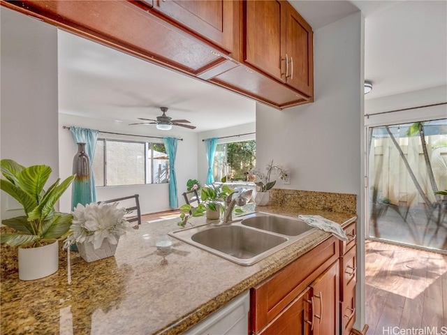 kitchen with ceiling fan, light stone counters, wood finished floors, a sink, and brown cabinetry