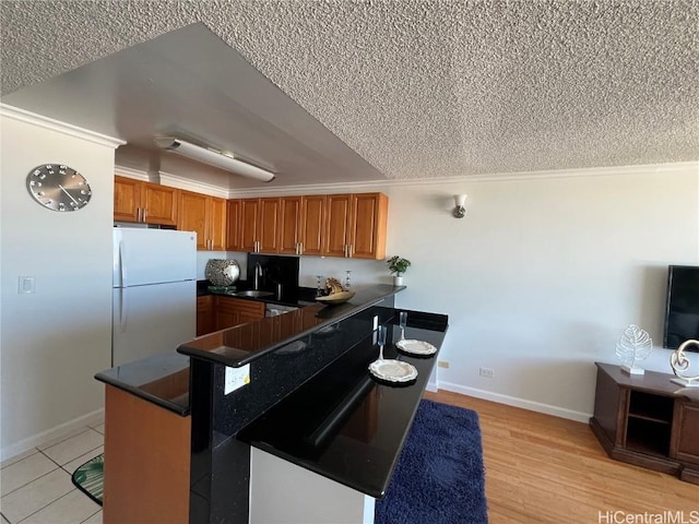 kitchen featuring sink, white fridge, ornamental molding, light wood-type flooring, and kitchen peninsula