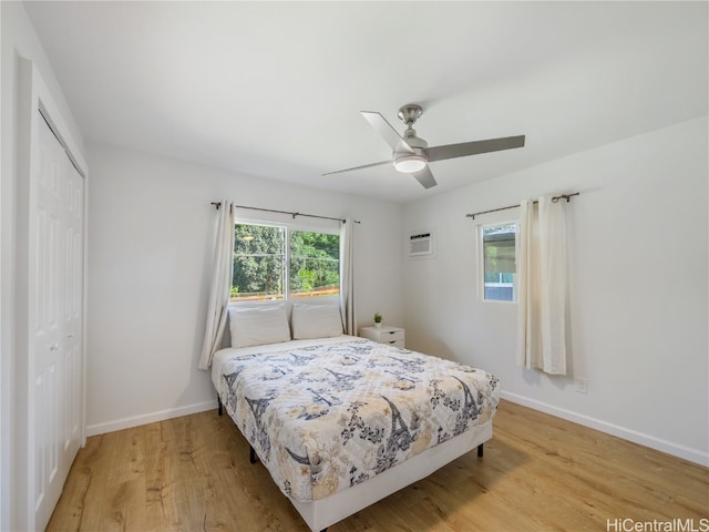 bedroom with light wood-type flooring, multiple windows, a closet, and an AC wall unit