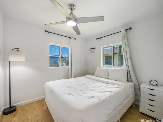 bedroom featuring multiple windows, light wood-type flooring, a wall unit AC, and baseboards