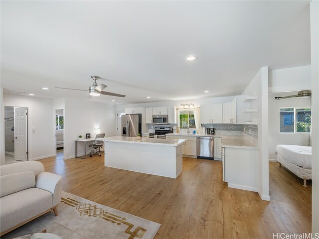 kitchen with appliances with stainless steel finishes, backsplash, white cabinets, a center island, and light hardwood / wood-style floors