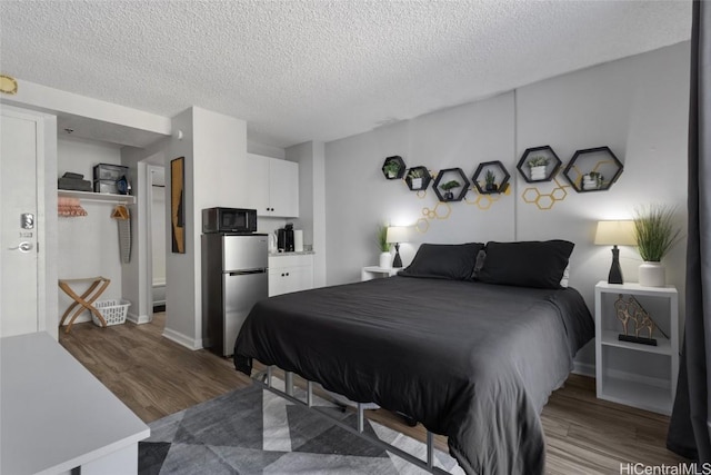 bedroom featuring wood-type flooring, a textured ceiling, and stainless steel refrigerator