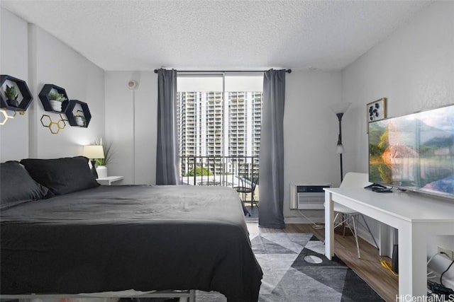 bedroom with hardwood / wood-style floors, a textured ceiling, an AC wall unit, and expansive windows