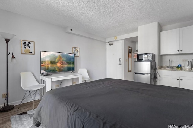 bedroom featuring stainless steel fridge, a textured ceiling, dark wood-type flooring, and sink