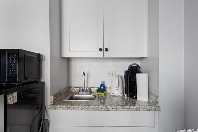 kitchen featuring light stone counters, sink, and white cabinets