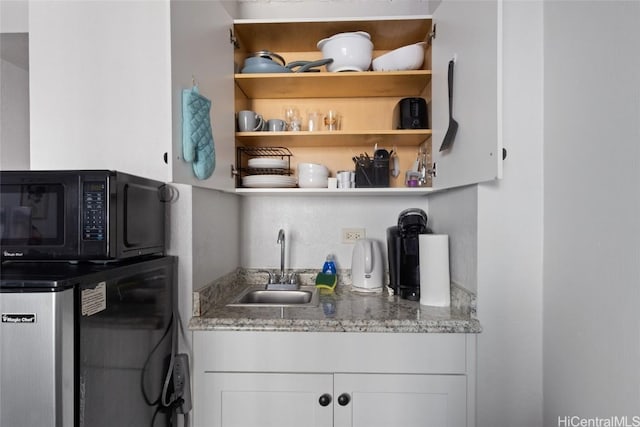 bar featuring white cabinets, stone counters, fridge, and sink