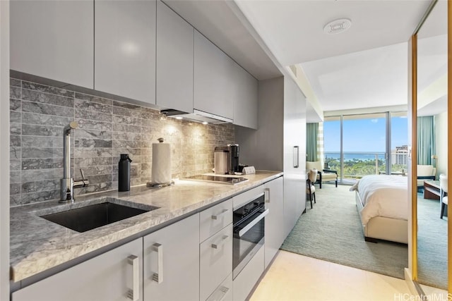 kitchen with light stone countertops, sink, expansive windows, backsplash, and oven