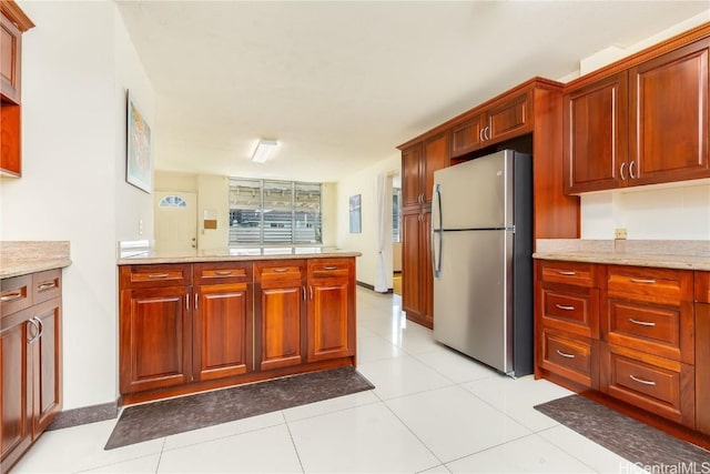 kitchen with light stone countertops, stainless steel refrigerator, and light tile patterned flooring