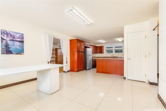 kitchen featuring kitchen peninsula, stainless steel fridge, light tile patterned floors, and sink