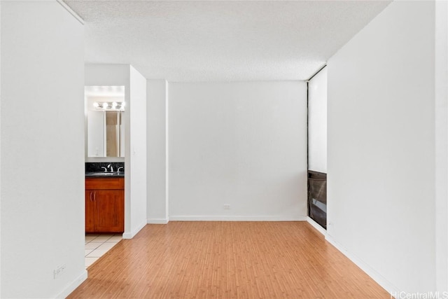 unfurnished room featuring sink, light hardwood / wood-style flooring, and a textured ceiling