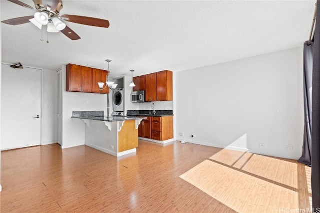 kitchen featuring a breakfast bar, ceiling fan, hanging light fixtures, stacked washer / drying machine, and light wood-type flooring