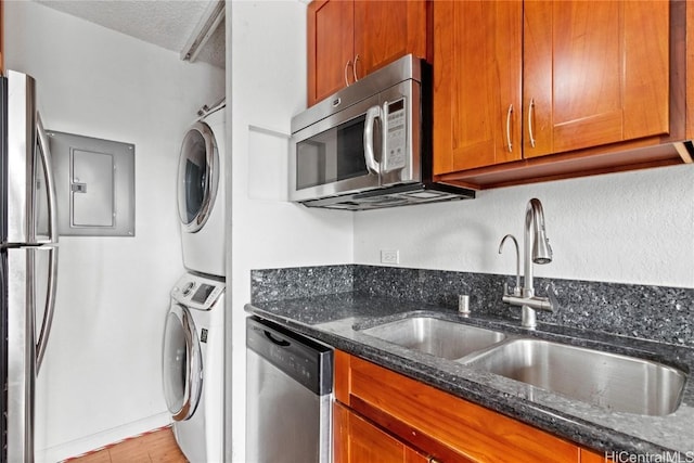 kitchen featuring sink, appliances with stainless steel finishes, stacked washer / drying machine, a textured ceiling, and dark stone counters