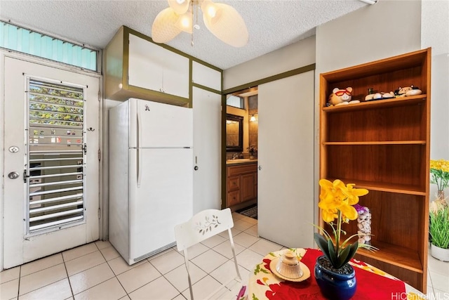 kitchen featuring white refrigerator, sink, ceiling fan, a textured ceiling, and light tile patterned flooring