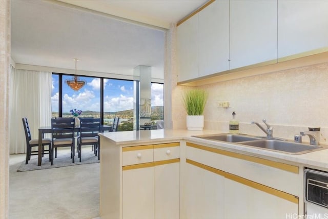 kitchen featuring kitchen peninsula, sink, decorative light fixtures, dishwasher, and white cabinets